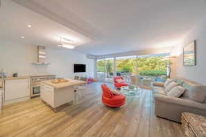 A modern living room with a kitchen, a red chair, a sofa, and a glass coffee table. - Charming Apartment With Pool 2br/4p - Saint-tropez (Saint-Tropez)