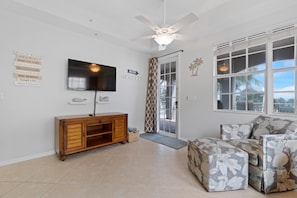A living room with a television, a ceiling fan, a sofa, and a window with a view. - White Cap Condo B201 (Fort Myers Beach)
