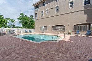 A swimming pool with a brick patio, lounge chairs, and a building with multiple windows and balconies. - White Cap Condo B201 (Fort Myers Beach)
