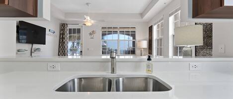 A modern kitchen with a stainless steel sink, wooden cabinets, a ceiling fan, and a large window.