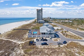Ein Strandhotel mit Pool, Parkplatz und einem hohen Gebäude im Hintergrund.