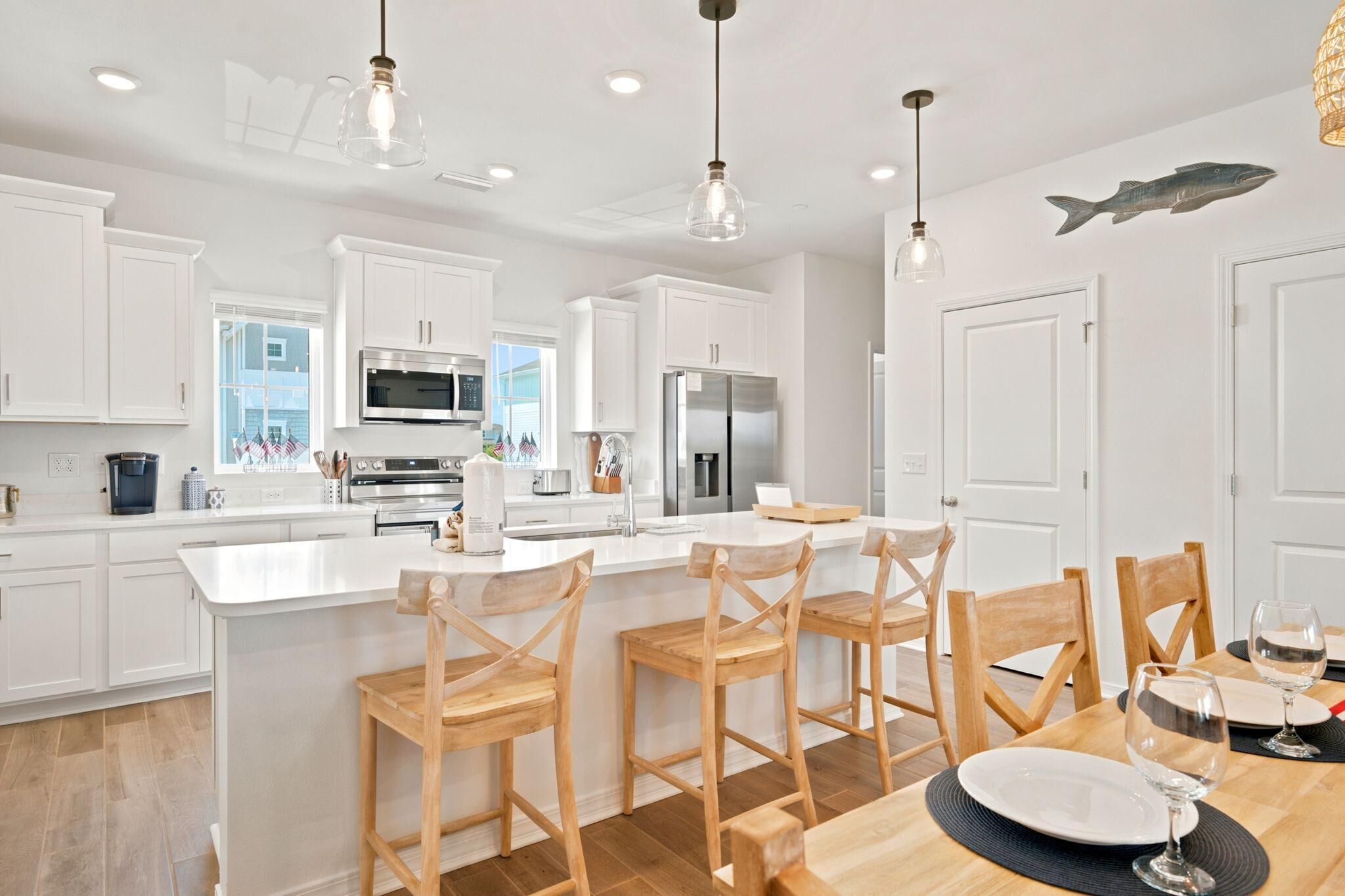 A modern kitchen with white cabinetry, stainless steel appliances, and wooden bar stools.
