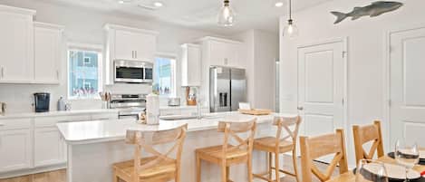 A modern kitchen with white cabinetry, stainless steel appliances, and wooden bar stools.