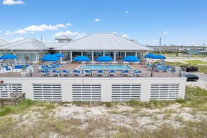 A poolside area with blue umbrellas, lounge chairs, and a building with a white roof. - Salty Turtle at Lost Key Villas (Pensacola)