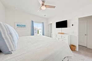 A bedroom with a bed, a ceiling fan, a TV, a window with curtains, and a door. - Salty Turtle at Lost Key Villas (Pensacola)