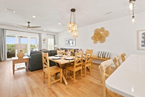 A dining area with a wooden table and chairs, a ceiling fan, and a wall-mounted light fixture. - Salty Turtle at Lost Key Villas (Pensacola)