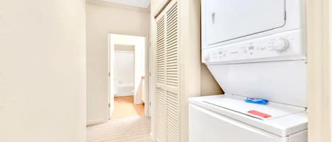 A laundry room with a washer and dryer, a door leading to another room, and a hallway with a carpeted floor.