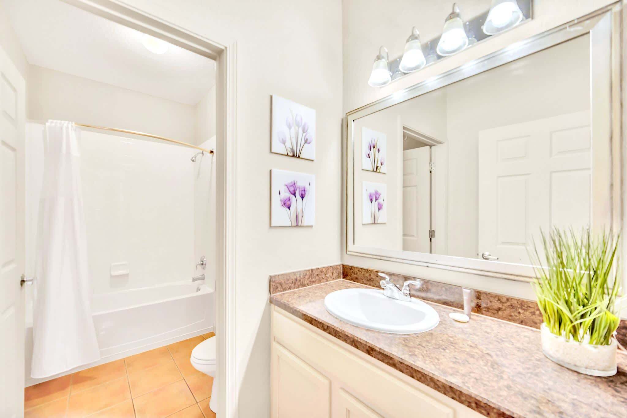 Un baño con bañera, inodoro, lavabo y un espejo grande con iluminación.