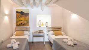 Ein Hotelzimmer mit zwei Betten, einem kleinen Tisch, einem Gemälde und einem Fenster mit Dekoration.