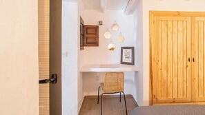 A room with a wooden door, a wicker chair, a white shelf with a framed picture, and hexagonal wall lights. - Peña de los Enamorados Antequera by Ruralidays (Málaga)