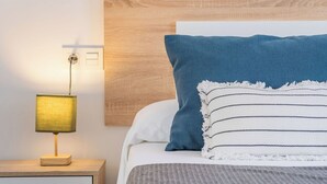 A neatly made bed with a blue pillow and a striped pillow, a bedside lamp, and a wooden headboard. - Oasis de Cáñar by Ruralidays (Granada)