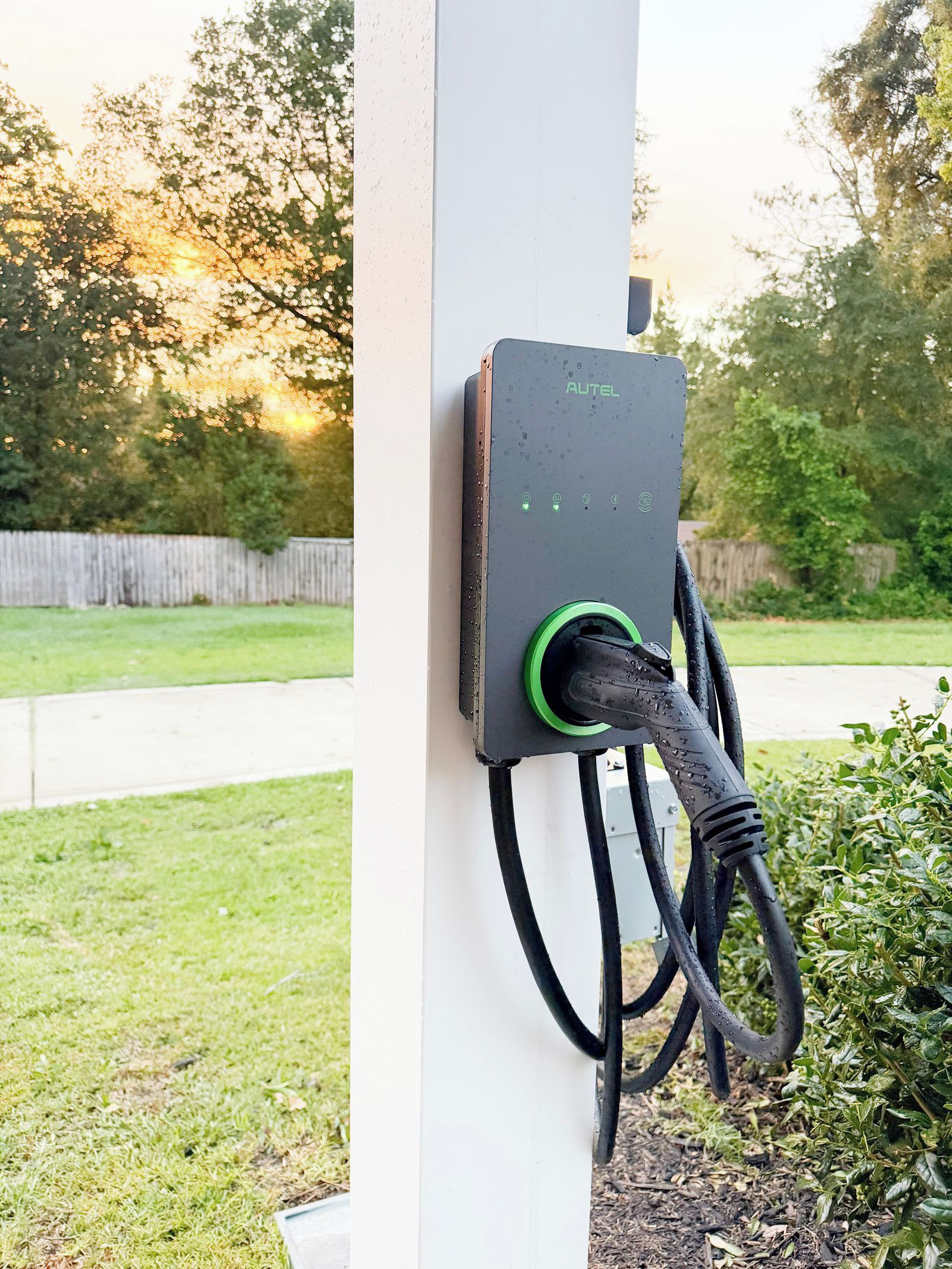 Een laadstation voor elektrische voertuigen buiten, met een kabel aangesloten, gemonteerd op een witte paal.