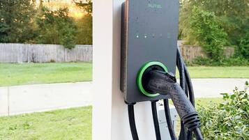 Een laadstation voor elektrische voertuigen buiten, met een kabel aangesloten, gemonteerd op een witte paal.