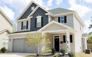 A two-story residential house with a garage, a covered porch, and a small tree in the front yard.