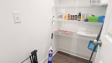 A compact storage area with shelves holding travel mugs, cleaning supplies, and a vacuum cleaner.