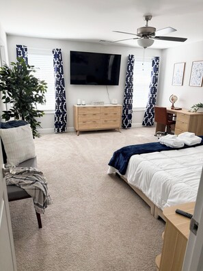 A bedroom with a bed, a dresser, a television, a ceiling fan, and a potted plant.