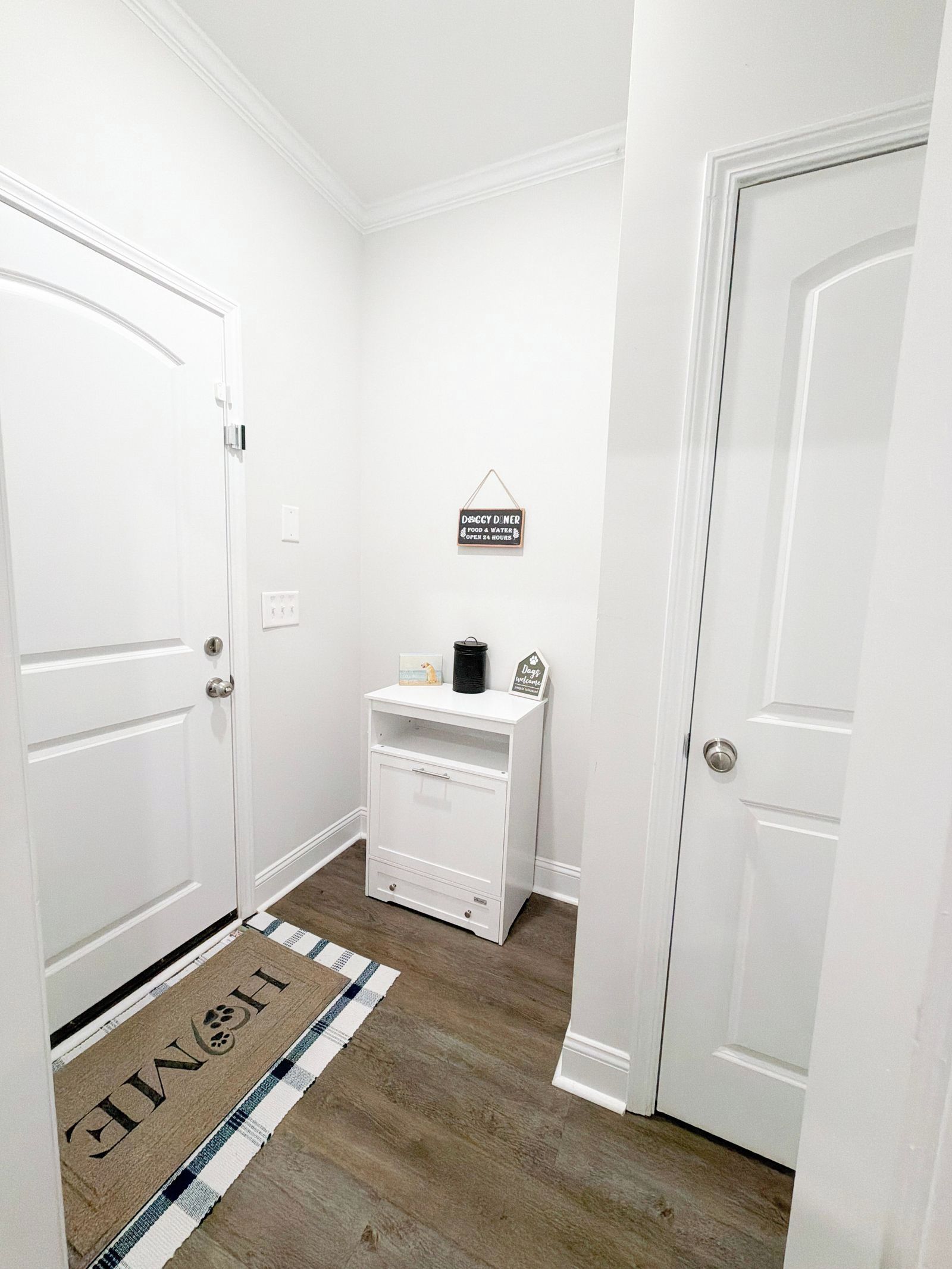 A hallway with white doors, a white cabinet, and a welcome mat.