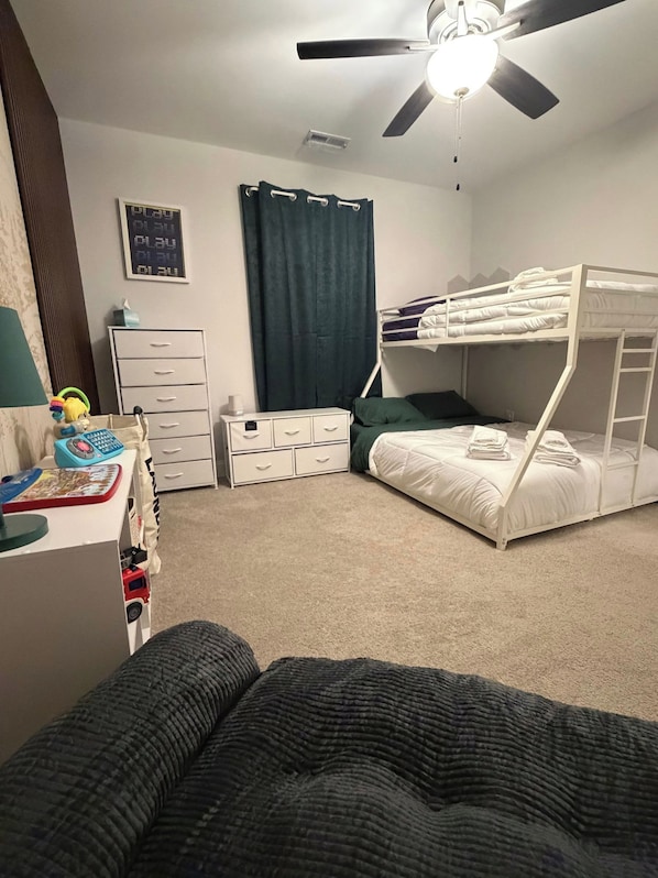 Un dormitorio con literas, un escritorio con silla, un ventilador de techo y una ventana con cortinas.
