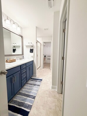 A hallway with a bathroom featuring a sink, mirror, and towel rack.