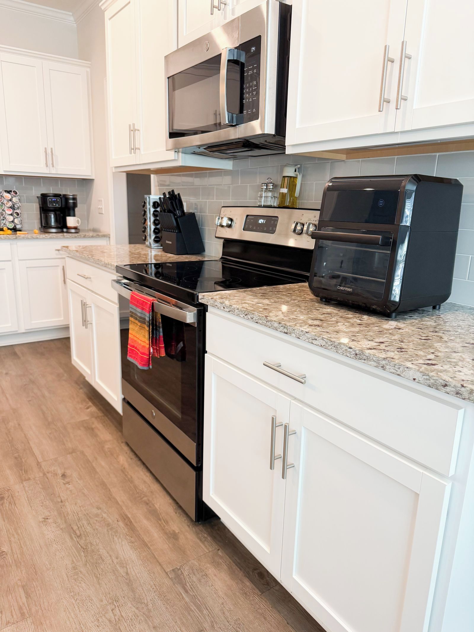 A kitchen with white cabinets, a stainless steel oven, a microwave, and a coffee maker.