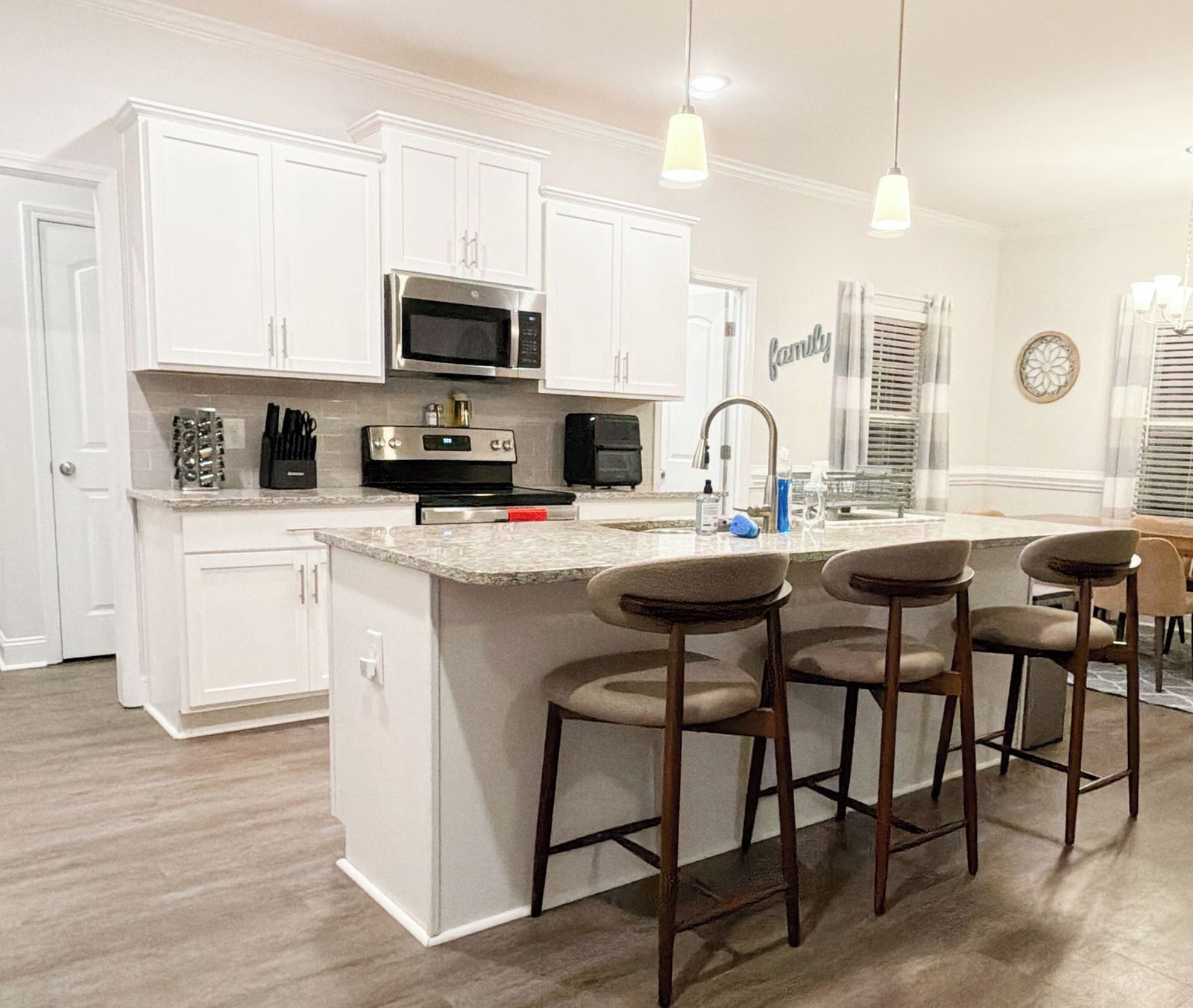 A kitchen with white cabinets, a stainless steel microwave, a sink, and a bar area with stools.