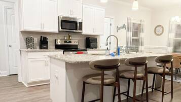 A kitchen with white cabinets, a stainless steel microwave, a sink, and a bar area with stools.