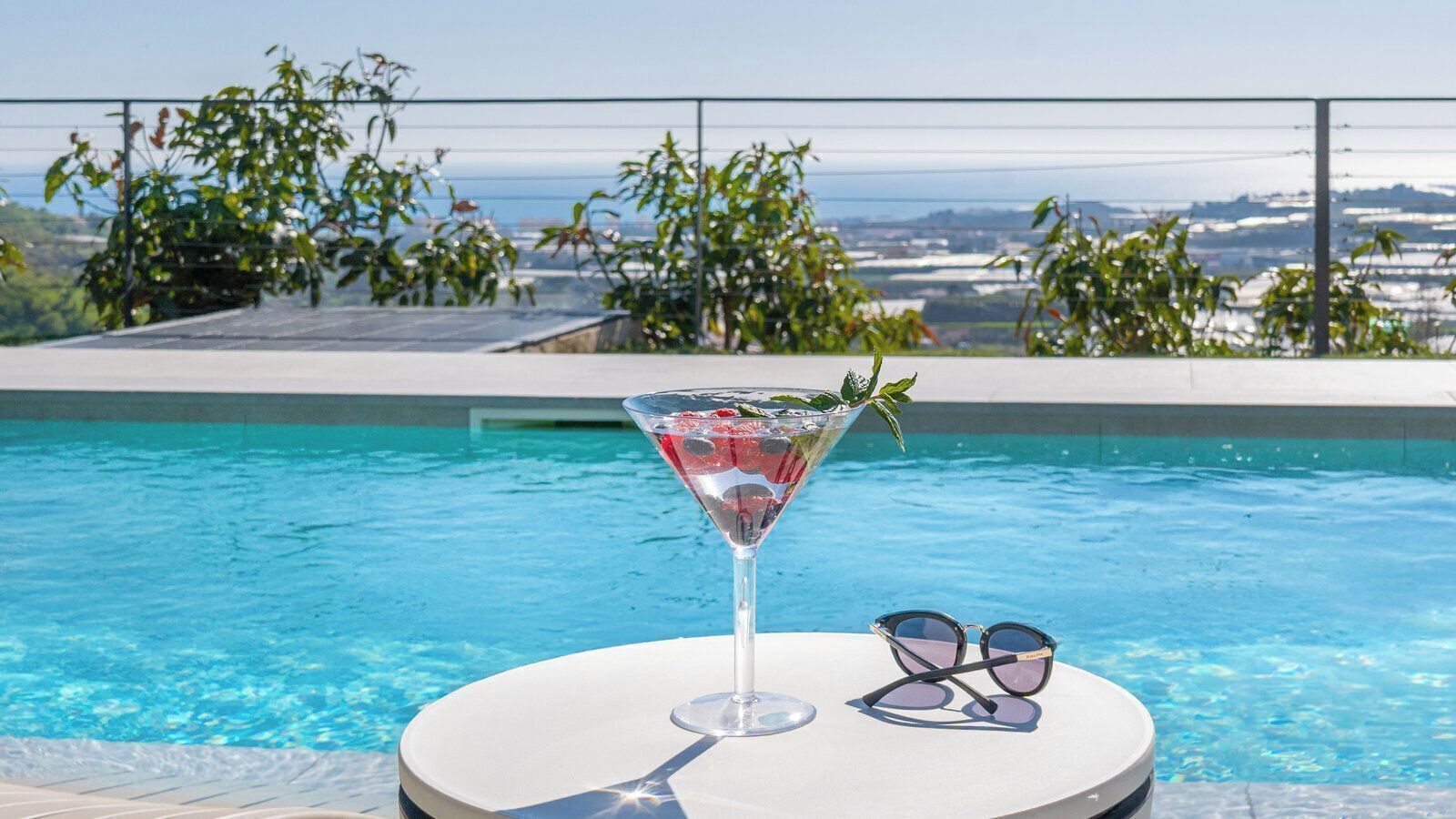 A poolside setting with a clear view of the ocean, a martini glass, and sunglasses on a table.