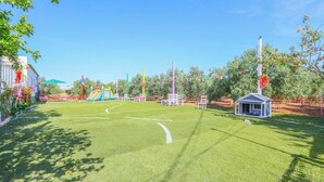 Un área verde bien cuidada con un pequeño pabellón, un parque infantil colorido y una zona vallada.