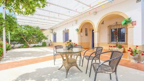 A covered patio with a glass table and wicker chairs, surrounded by potted plants and a tiled floor. - La Casa del Flamenco Fuente Palmera by Ruralidays (Sevilla)