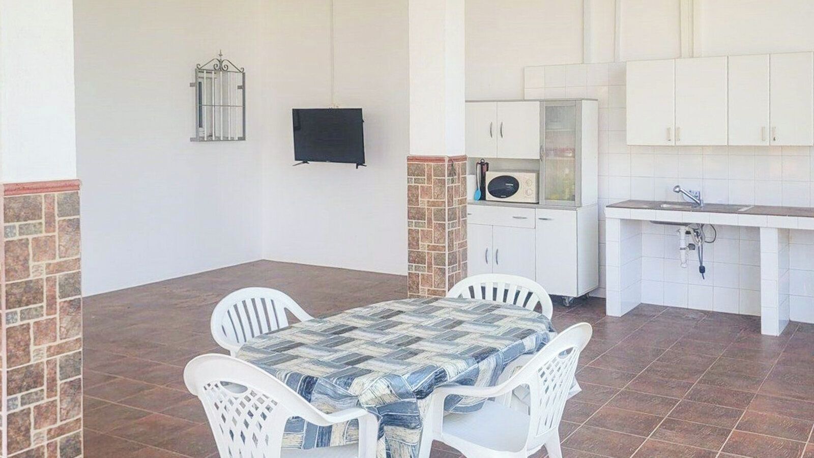 A patio with a table and chairs, a kitchen area with cabinets and a microwave, and a tiled floor.