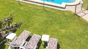 Un espace piscine comprenant quatre chaises longues et une petite table, le tout entouré d’une pelouse bien entretenue.