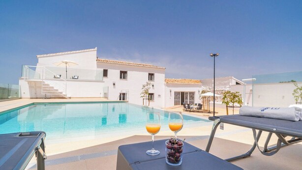 Zona de piscina con vista despejada a un edificio, una silla de descanso y una mesa con bebidas y fruta.