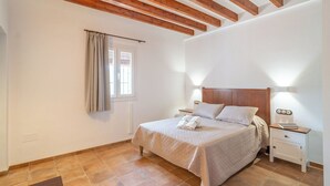 Un dormitorio con cama, mesitas de noche, una ventana con cortinas y vigas de techo de madera.