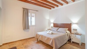 A bedroom with a bed, bedside tables, a window with curtains, and wooden ceiling beams. - Cortijo La Alcaidía Archidona by Ruralidays (Málaga)