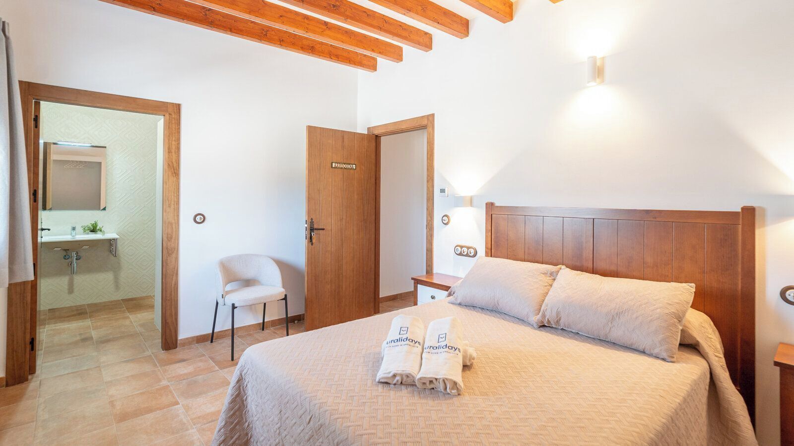 Een hotelkamer met een bed, een stoel, een nachtkastje en een deur naar een badkamer.