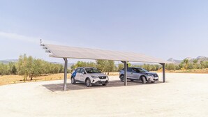 Dos autos estacionados bajo una estructura de paneles solares en un paisaje desértico.