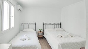 A hotel room with two single beds, a small table with a plant, and an air conditioning unit. - Casa del Tío Paco Montecorto by Ruralidays (Málaga)