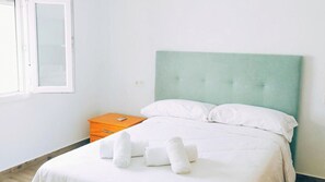 A neatly made bed with white linens and pillows, a wooden nightstand with a remote control, and a window with frosted glass. - Casa del Tío Paco Montecorto by Ruralidays (Málaga)