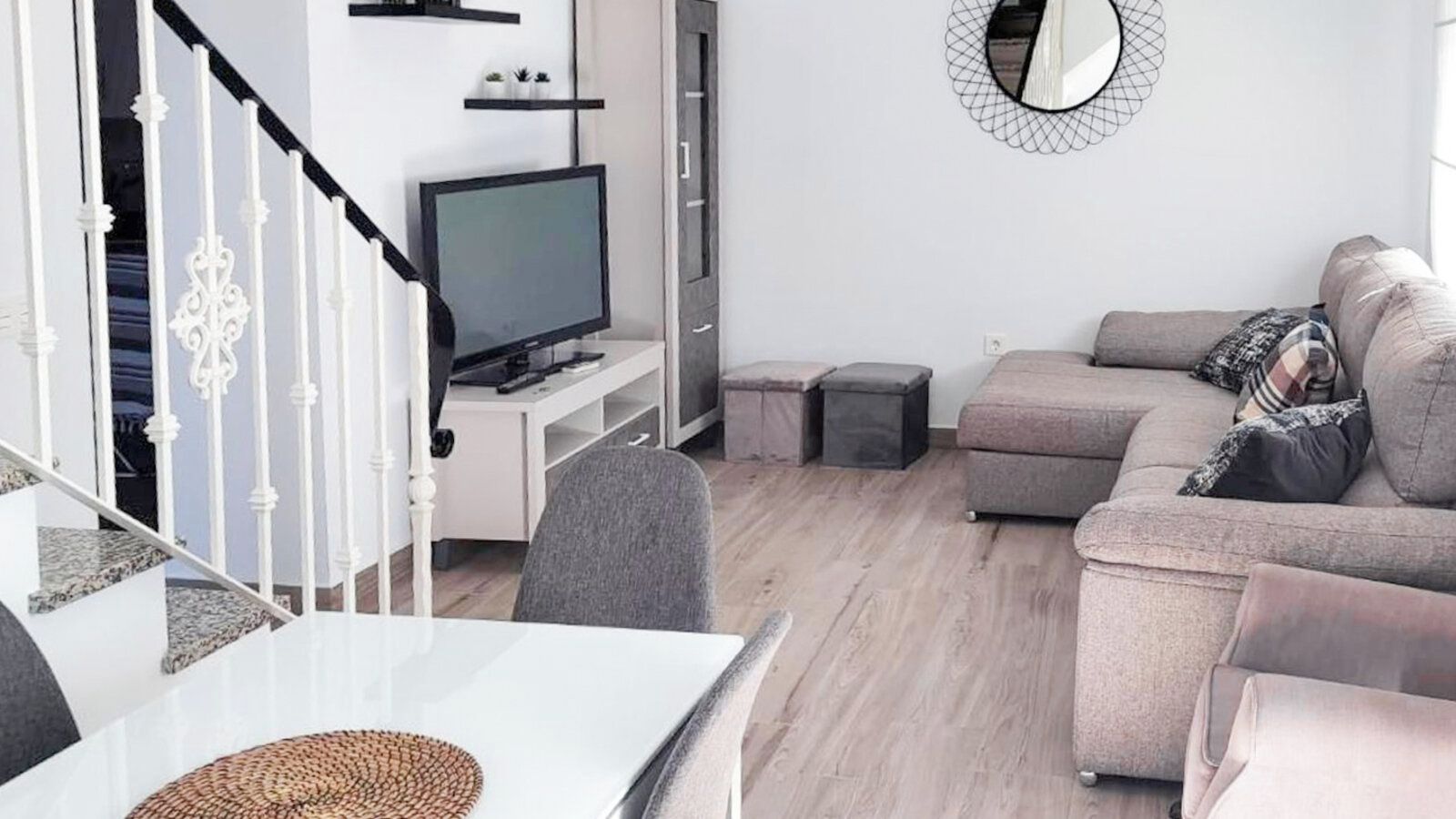 A modern living room with a flat-screen TV, a grey sofa, and a dining area with a white table.