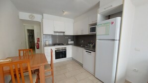 A compact kitchen with white cabinets, a stove, a microwave, and a refrigerator. - Apartment 'Nou 8' with Balcony, Wi-Fi and Air Conditioning (Sitges)