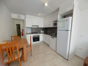 A compact kitchen with white cabinets, a stove, a microwave, and a refrigerator. - Apartment 'Nou 8' with Balcony, Wi-Fi and Air Conditioning (Sitges)