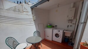 A small outdoor kitchen area with a washing machine, a sink, and a table with chairs. - Apartment 'Nou 8' with Balcony, Wi-Fi and Air Conditioning (Sitges)