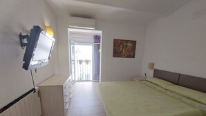A bedroom with a bed, a TV mounted on the wall, a radiator, a door leading to a balcony, and a painting on the wall. - Apartment 'Nou 8' with Balcony, Wi-Fi and Air Conditioning (Sitges)
