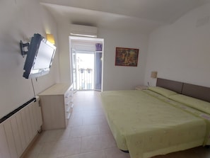 A bedroom with a bed, a TV mounted on the wall, a radiator, a door leading to a balcony, and a painting on the wall. - Apartment 'Nou 8' with Balcony, Wi-Fi and Air Conditioning (Sitges)