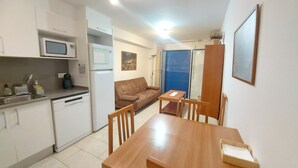 A compact kitchen with a microwave, refrigerator, and coffee maker. There's a dining area with a wooden table and chairs. - Apartment 'Nou 8' with Balcony, Wi-Fi and Air Conditioning (Sitges)