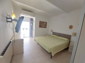 A bedroom with a bed, a nightstand, a wall-mounted lamp, a painting, and a sliding door leading to a balcony. - Apartment 'Nou 8' with Balcony, Wi-Fi and Air Conditioning (Sitges)