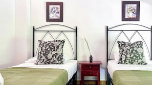 Two twin beds with floral-patterned pillows, a small bedside table with a vase, and framed artwork on the wall. - Casa Viladán Colmenar by Ruralidays (Málaga)