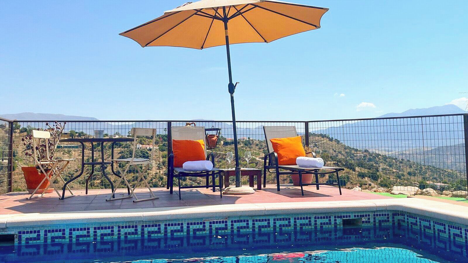 Un espace aménagé au bord de la piscine, avec des chaises longues, un parasol et une vue sur le paysage.