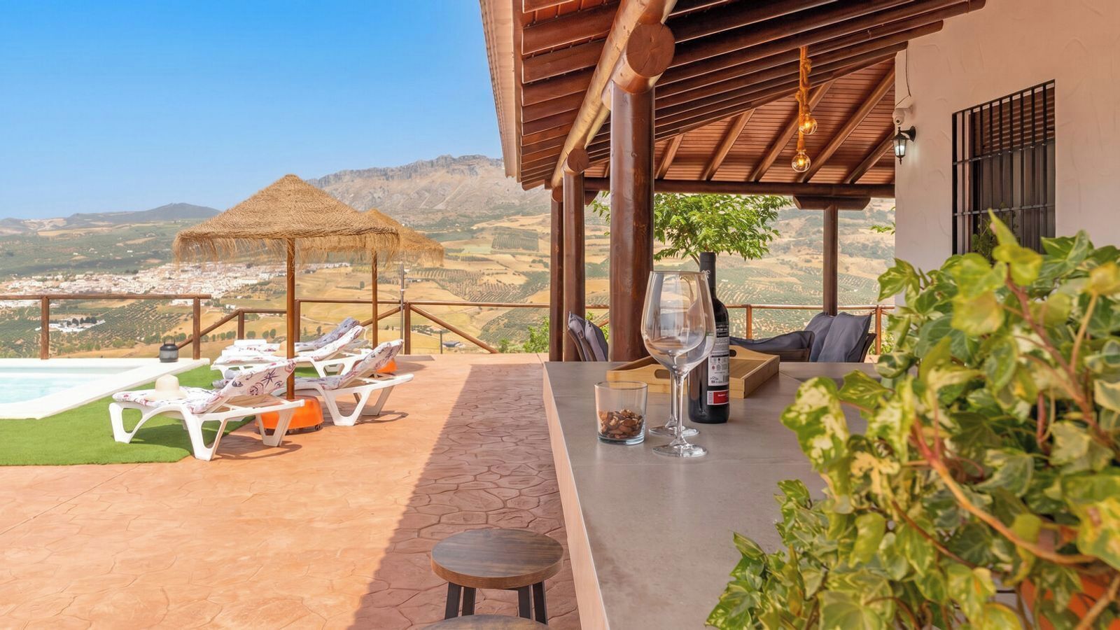 A terrace with lounge chairs, a table with a wine glass and bottle, and a view of the landscape.