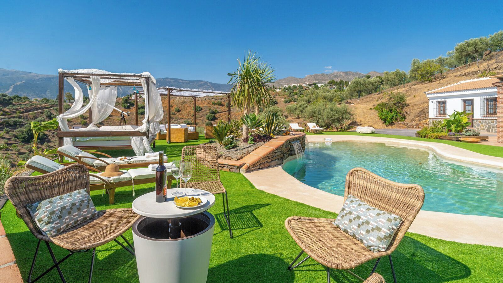 Un espace aménagé au bord de la piscine, avec des meubles en osier, une pergola et une vue sur les collines.